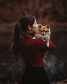 a woman is holding a small dog in her arms while she looks into the distance