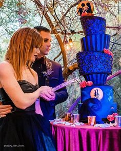 a man and woman standing in front of a blue cake on top of a table