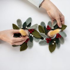 two hands are making christmas wreaths out of felt and wood beads on a white surface