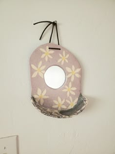 a mirror hanging from the side of a wall with flowers painted on it and black string