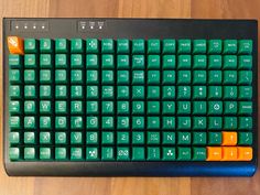 a computer keyboard sitting on top of a wooden table with orange and green keys in front of it