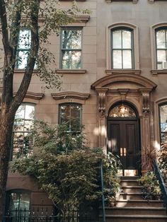 an apartment building with stairs leading up to the front door and trees on either side