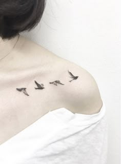 a woman's shoulder with three birds flying in the sky on her left side