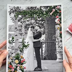 two hands holding up a photo of a bride and groom in front of a tree