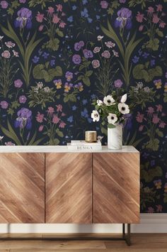 a sideboard with flowers on it in front of a wallpapered background and wooden cabinet