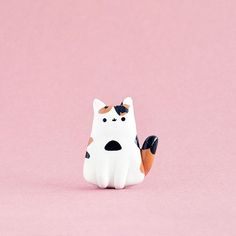 a small white and brown cat figurine on a pink background