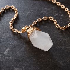 a gold chain with a white quartz stone on it's end, sitting on a black surface