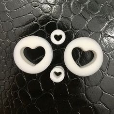 three white heart shaped buttons sitting on top of a black leather surface with two hearts in the middle