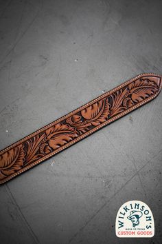 a brown leather belt with an intricate design on the front and side, sitting on a gray surface