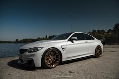 a white car parked next to a body of water with gold rims on it