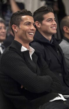 two men sitting next to each other in front of a crowd at a fashion show