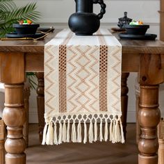 a table topped with a black vase and a white table runner on top of a wooden table