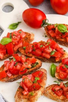 toasted bread with tomatoes and basil on top sitting on a white plate next to some fresh cherry tomatoes