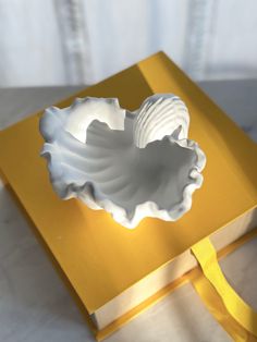 a yellow box with a white shell in it and a ribbon on the side that is attached to it