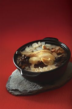 a black bowl filled with rice and meat on top of a red table next to a rock