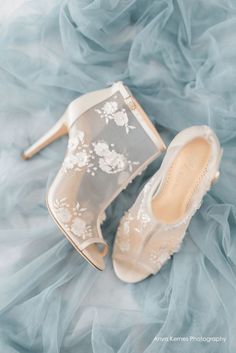 a pair of wedding shoes on top of a blue cloth covered bed sheet with white flowers