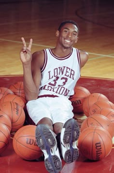 a basketball player sitting on the floor with his hands up and two orange balls in front of him