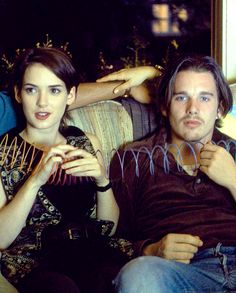 three people sitting on a couch with one holding something in his hand and the other looking at the camera