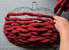 someone is making a knitted basket out of red yarn and scissors on a cutting board