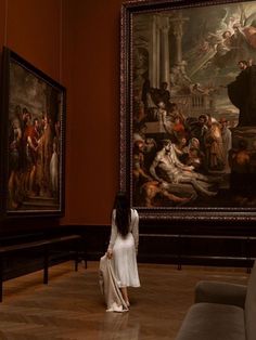 a woman is standing in front of two paintings on the wall and looking at them