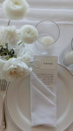 a table setting with white flowers and silverware on it, including a napkin that says casie