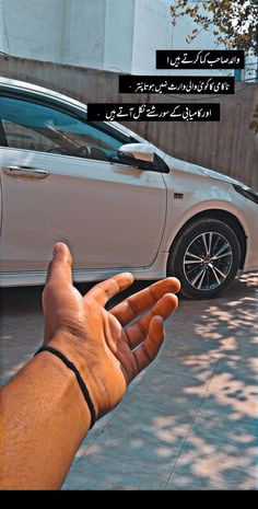 a person holding their hand out in front of a white car with arabic writing on it