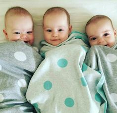 three babies wrapped up in blankets on top of a bed with white and blue polka dots