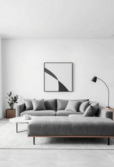 living room with a monochrome grey palette. The room includes a low-profile grey sofa, geometric wall art, and simple furniture with clean lines. White and light grey walls, a neutral-toned rug, and sleek lighting contribute to the calm, uncluttered aesthetic. Sleek Lighting, Grey Palette, Simple Furniture, Geometric Wall Art