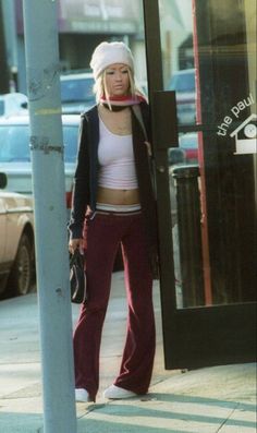 a woman standing next to a pole on the sidewalk with her hands in her pockets