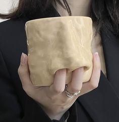 a woman in a black suit holding a beige square shaped object with her hands on it