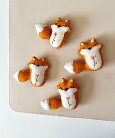 four little felt fox brooches on a white tablecloth with orange and white flowers