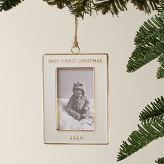 a baby's first christmas ornament hanging on a tree branch with pine needles