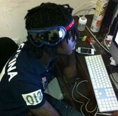 a man wearing goggles sitting in front of a computer desk with a keyboard and monitor