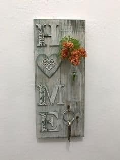 a wooden sign with flowers and a key hanging from it's side on the wall