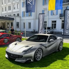 two silver sports cars parked in front of a large white building with blue and yellow flags