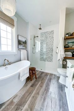 a white bathroom with wood flooring and large bathtub