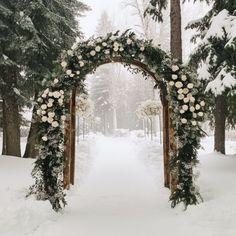 an archway decorated with flowers and greenery stands in the middle of a snowy forest