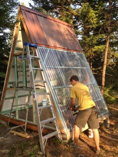 a man standing next to a tall metal structure in the middle of a forest on top of a ladder