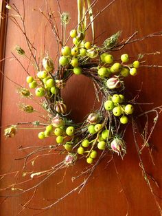 a wreath is hanging on the door with green berries and flowers attached to it's sides