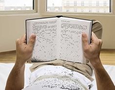 a man laying on his back reading a book with black speckles all over it