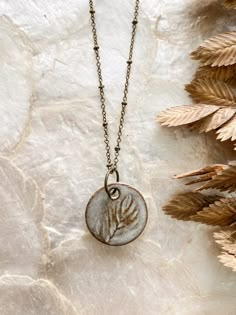 a necklace with a handprint on it sitting next to some dried plants and leaves