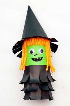 a green and black paper doll with orange hair wearing a witches hat on it's head