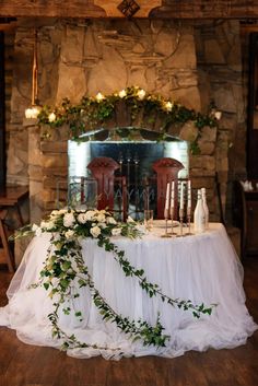 a table with flowers and candles on it in front of a fire place that is decorated with greenery