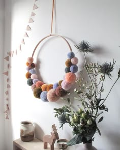 a wreath with pom - poms hangs on the wall next to a potted plant