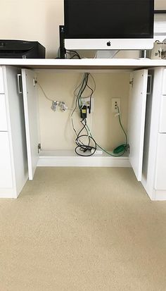 an office desk with two computers on it and wires running through the cabinet doors,