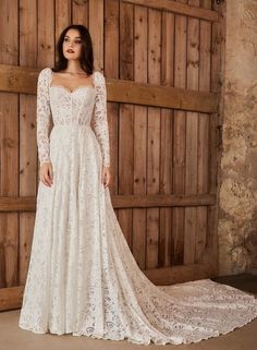 a woman in a white wedding dress standing next to a wooden wall wearing a long sleeved gown