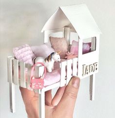 a hand holding a doll house with a horse on the bed and other toys in it