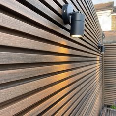 an outdoor wall light mounted on the side of a wooden slatted fence next to a house