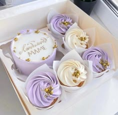 four cupcakes with frosting and gold decorations in a box on a table