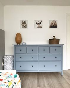 a blue dresser in a white room with pictures on the wall